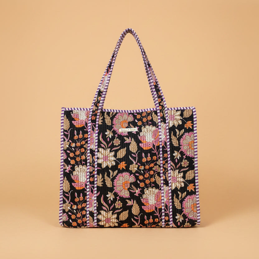 A large tote bag with a black background and colorful floral embroidery, hanging on a wooden display stand inside a toy and home goods store.