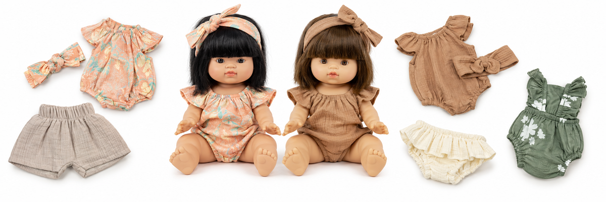 Minikane Jade and Jeanne dolls dressed in floral and hazelnut rompers, surrounded by doll clothing on white