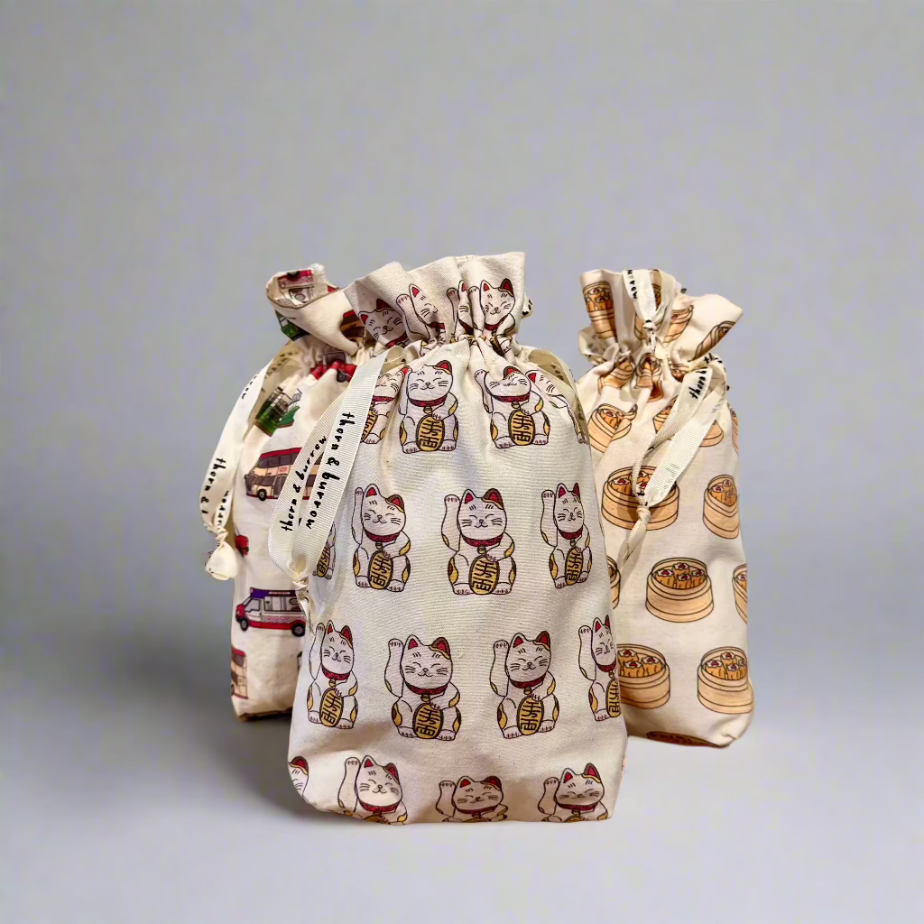 Gathered drawstring gift bags featuring Hong Kong transport, lucky cat and dim sum prints.