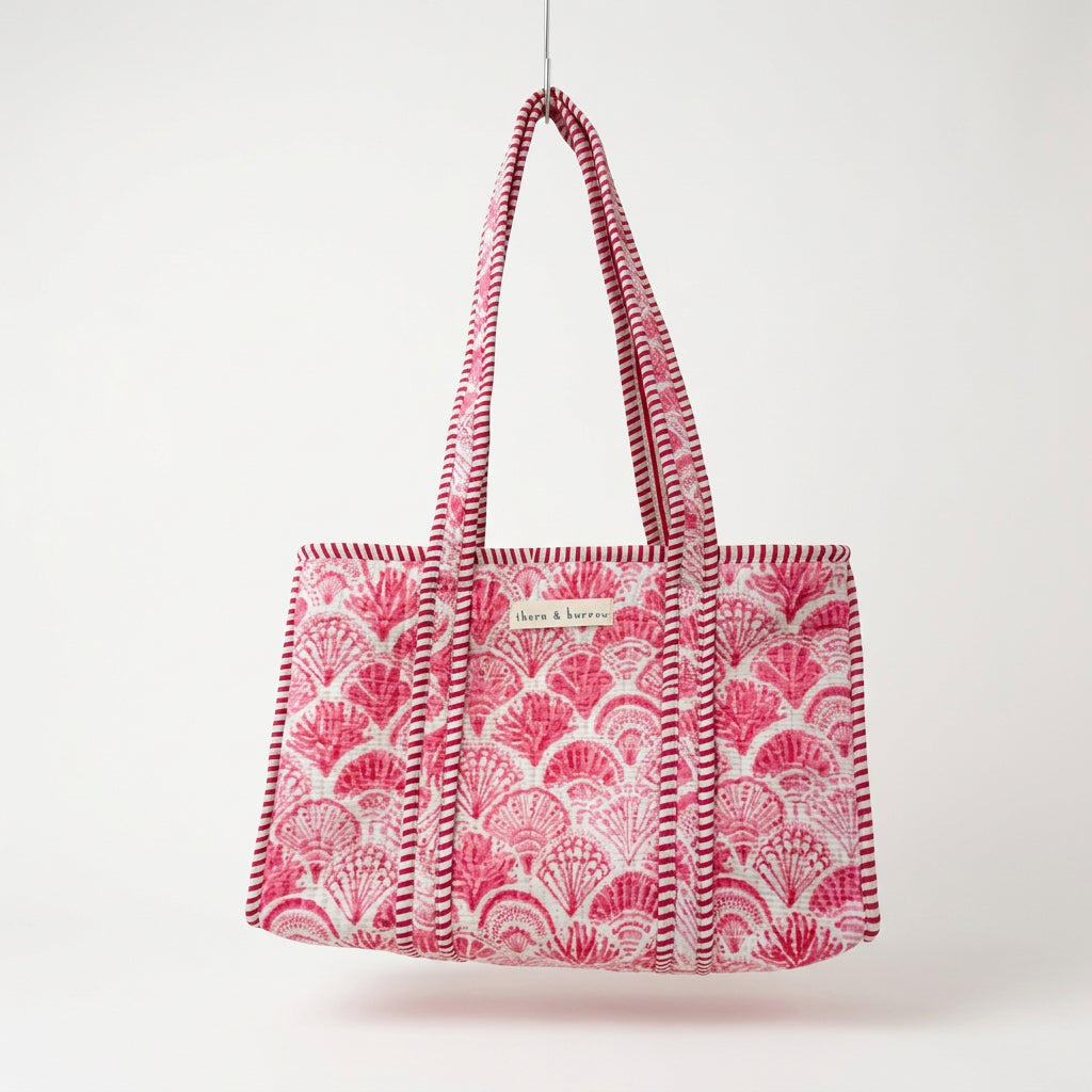 A pink and white patterned tote bag with woven shoulder straps, hanging from a gold hook in a retail store display.