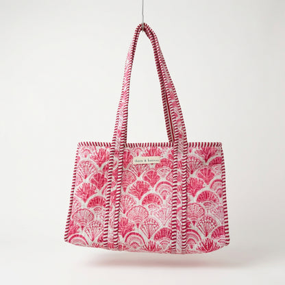 A pink and white patterned tote bag with woven shoulder straps, hanging from a gold hook in a retail store display.