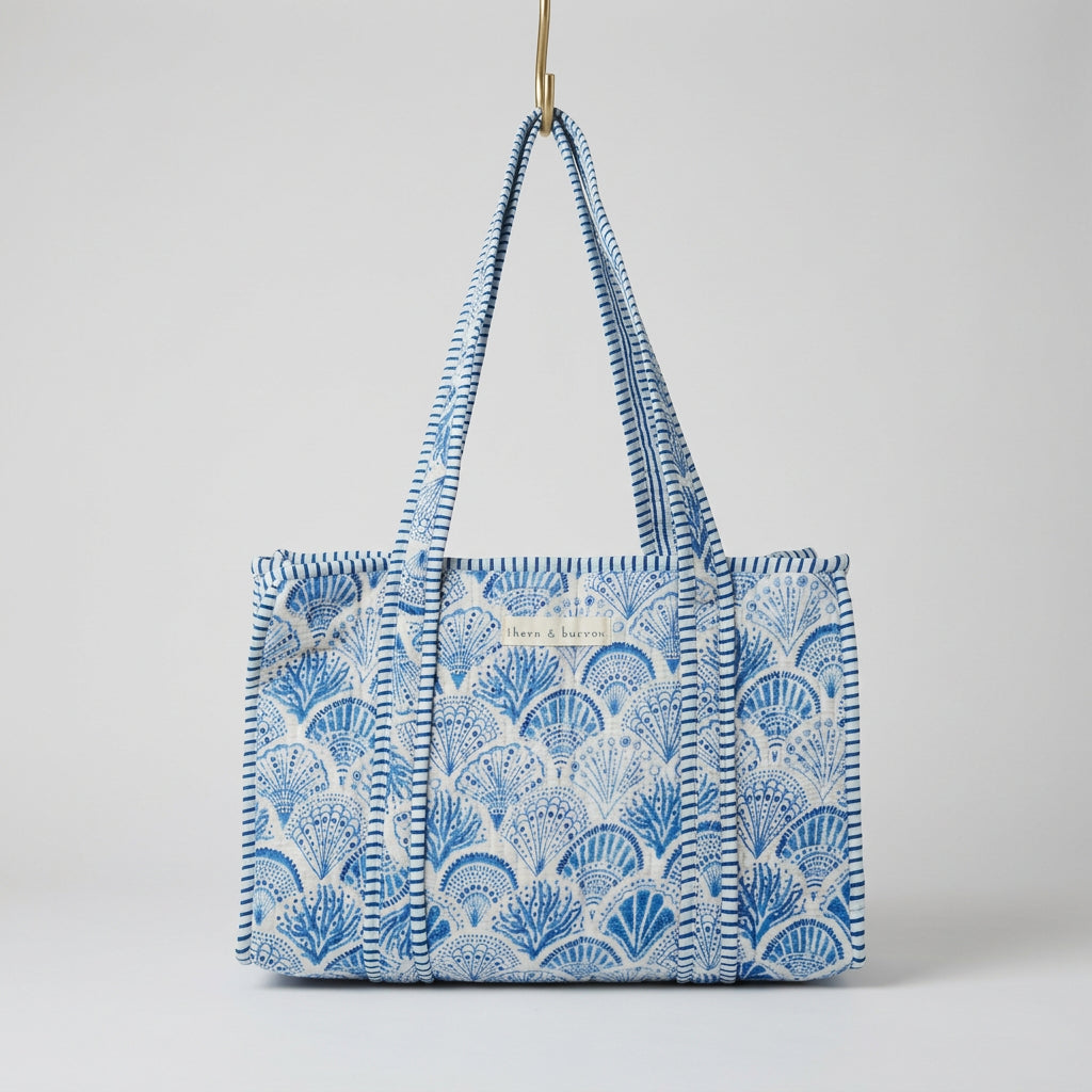 A blue and white patterned tote bag with braided shoulder straps, hanging in a retail store aisle.