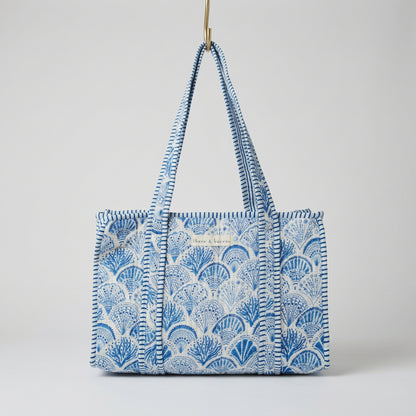 A blue and white patterned tote bag with braided shoulder straps, hanging in a retail store aisle.