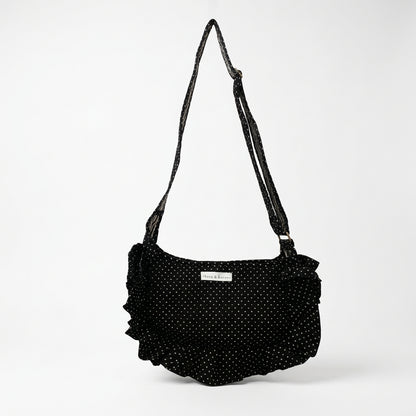 A black fabric shoulder bag with white polka dots hangs from a white metal display stand inside a retail store. 